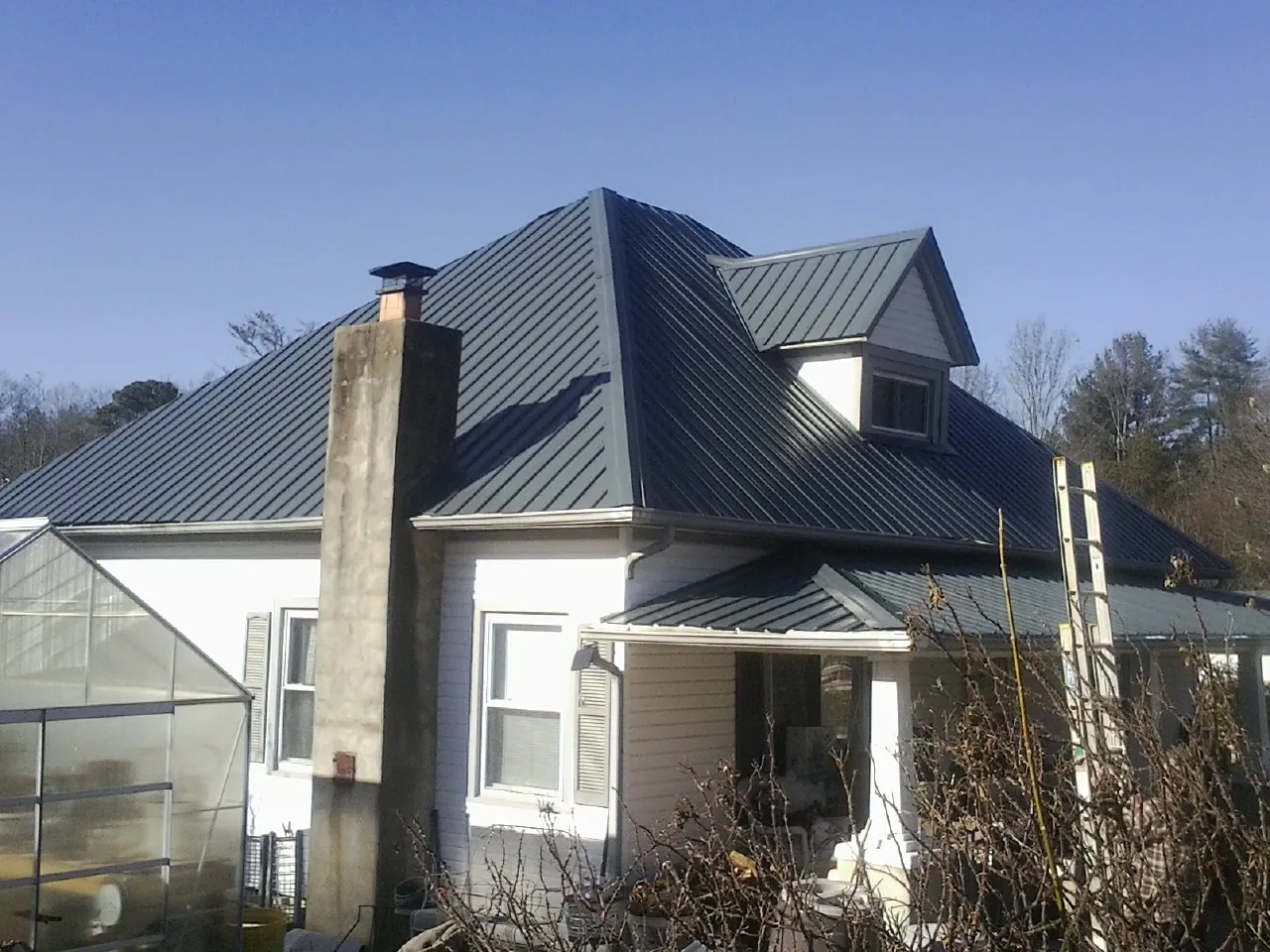 Dark blue standing seam metal roof on a white farmhouse with dormer — Slate & Tile Roof Repair by Roofing Brothers in Loysville