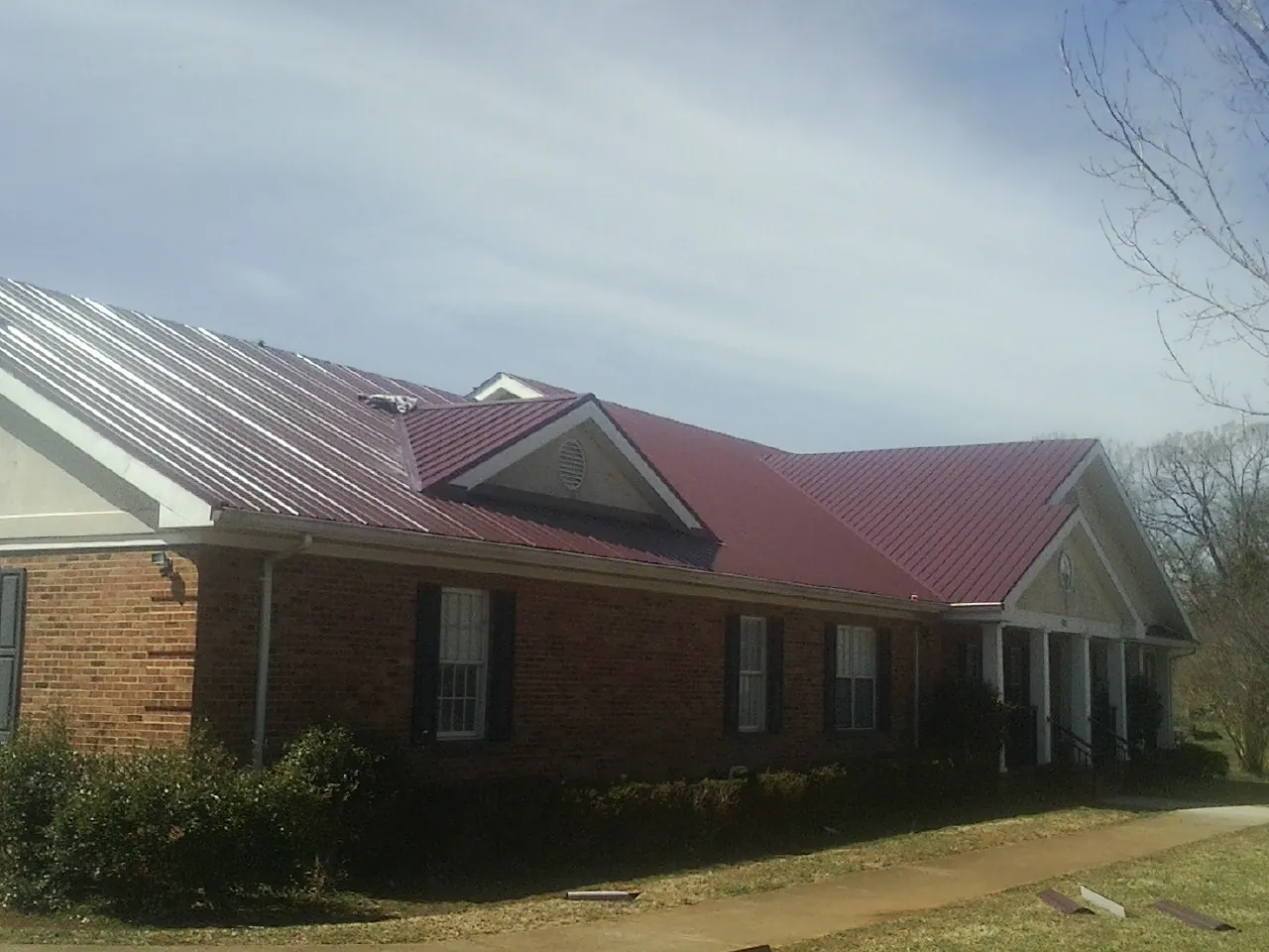 Red metal roof with gabled entries on a long brick building, from a Hail Damage Roof Repair job in Loysville
