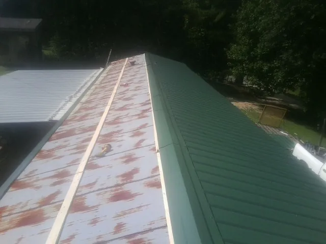 Old rusted panels beside newly installed green metal roofing — Wind Damage Roof Repair by Roofing Brothers in Loysville