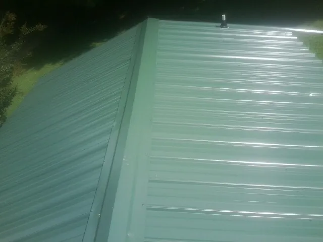 New green metal panels meeting at the ridge of a roof — Flat Roof Repair work by our crew in Loysville