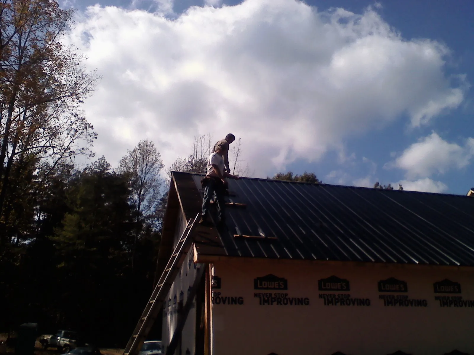 Roofer fastening dark metal panels high against a cloudy sky, from a Roof Inspection job in Loysville