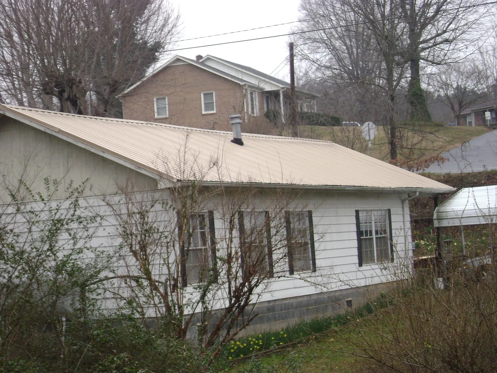 Tan metal roof on a white sided house set into a hillside — Commercial Roofing by Roofing Brothers in Loysville